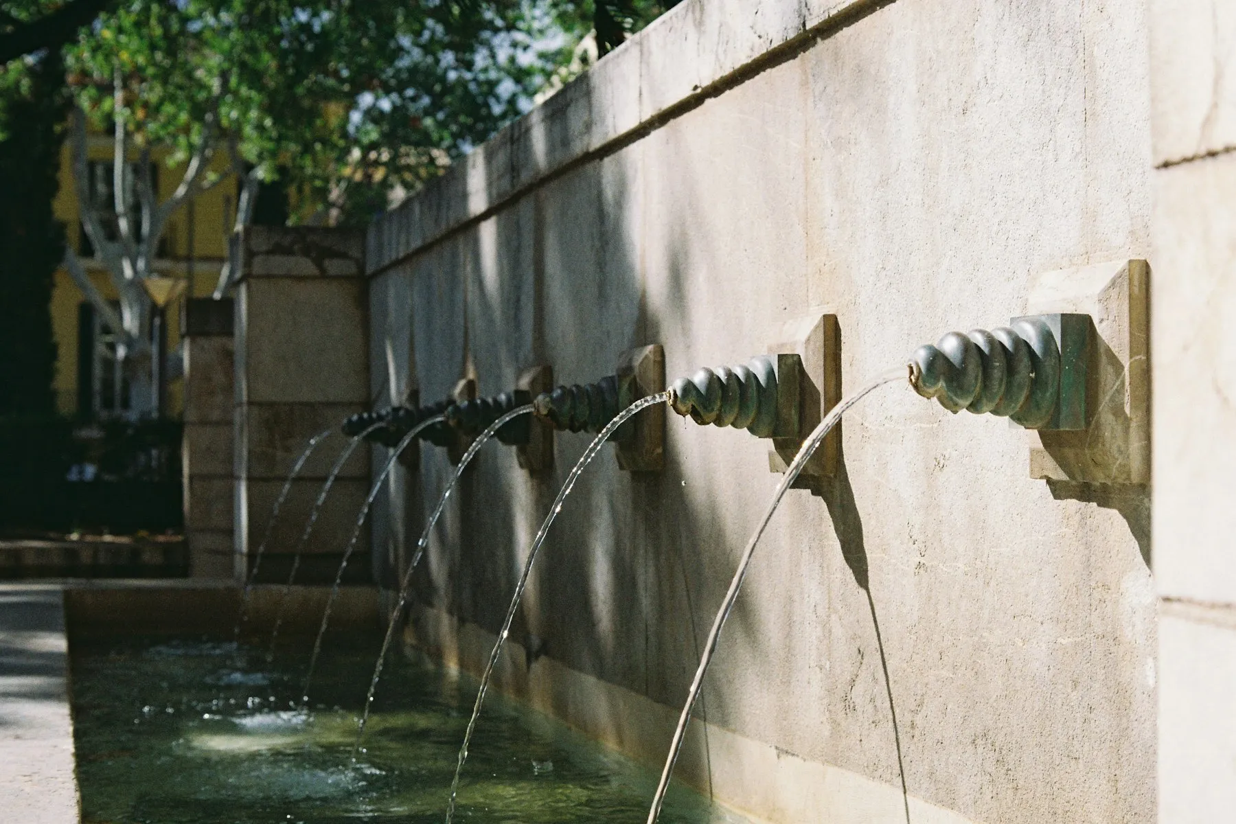 A stone wall water feature with spouts running into a pool
