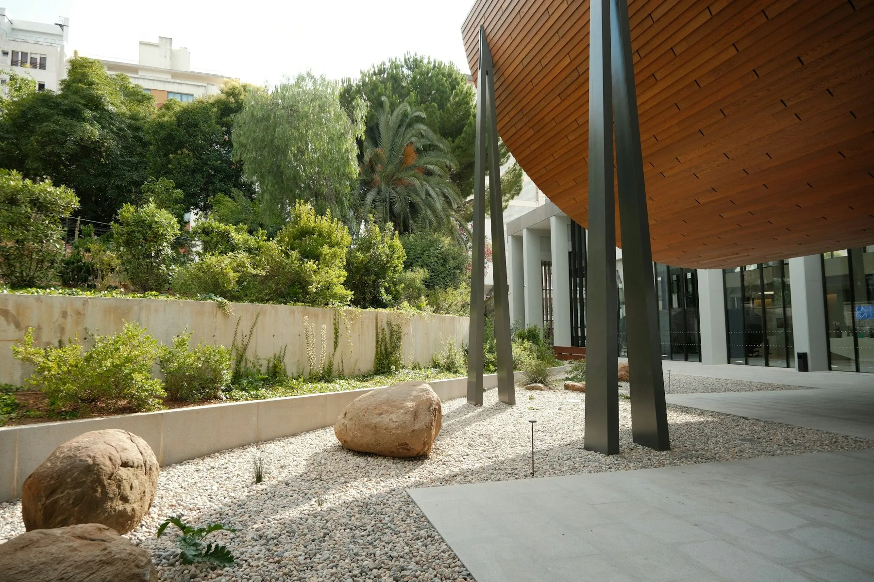 A gravel garden with boulders and trees at a modern building entrance